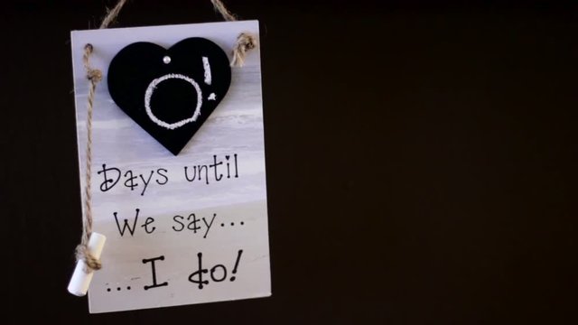 Sign with the text "0 Days until we say I do" hanging on a wall.