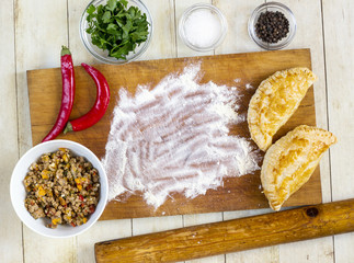 Empanadas cooking preparations: flour with spices, culinary herbs and minced pork on wood board