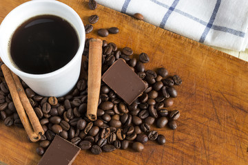 Coffee in white plastic glass with background of coffee beans, chocolate chunks and cinnamon sticks
