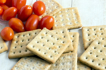 Cherry tomatoes with crackers on light wood background