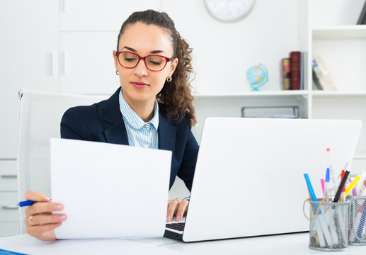 Smiling woman working with paperwork and laptop