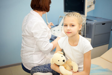 The girl with a soft toy in the hospital on a background of ultrasound machines, smiling and playing