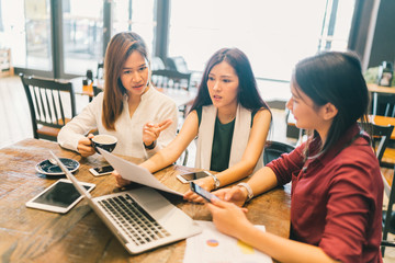 Group of young Asian women or college students in serious business meeting or project brainstorm discussion at coffee shop with laptop computer, tablet, and smartphone. Startup or teamwork concept
