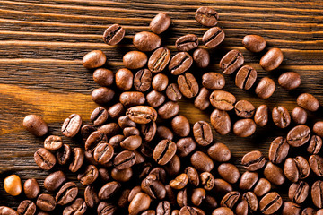 Macro image of roasted coffee beans at brown textured wooden board background.