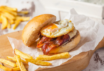 Hamburger with fried egg, bacon and french fries.