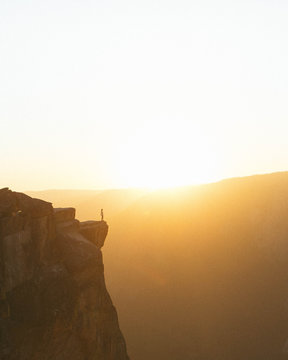 Person standing on edge of cliff at sunset 