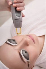 Therapist beautician makes a laser treatment to young woman's face at beauty SPA clinic.