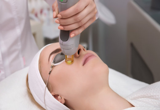 Therapist beautician makes a laser treatment to young woman's face at beauty SPA clinic.