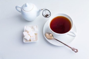 Cup of black tea, teapot with strainer and white sugar cubes.