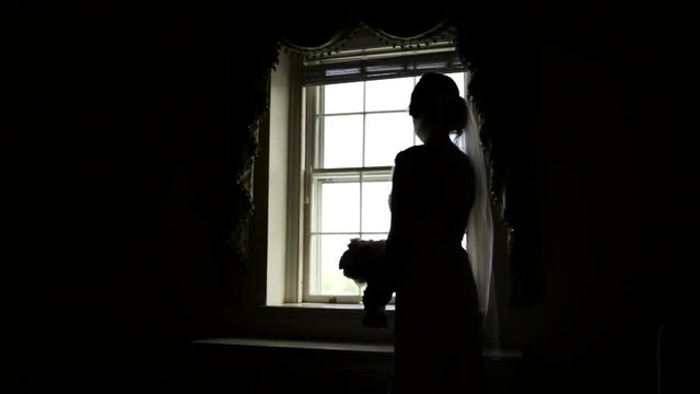 Silhouette of bride besides a window with her wedding bouquet