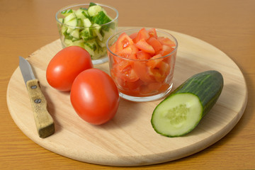 Whole cucumbers, tomatoes and salad of them on a cutting board.
