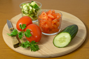 Whole cucumbers, tomatoes and salad of them on a cutting board.