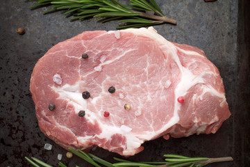 Raw pork steak on black rustic metal background with herbs and spices.