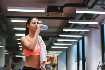 Woman drinking water after training in gym.