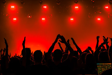 Fototapeta premium Silhouettes of people in a bright in the pop rock concert in front of the stage. Hands with gesture Horns. That rocks. Party in a club. Red background.
