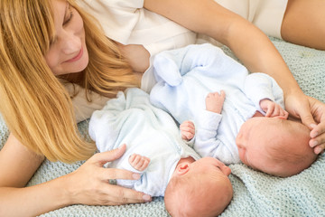 Obraz na płótnie Canvas young loving mother with newborn twin babies, indoor portrait