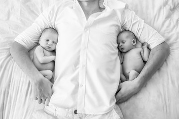 young loving father with newborn twin babies, indoor portrait