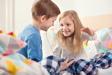 Two happy siblings children having fun and listening music with headphones in bed