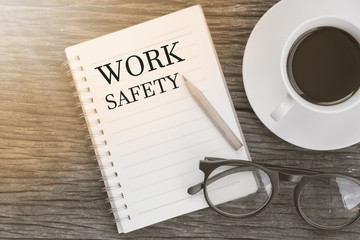 Concept Work safety message on notebook with glasses, pencil and coffee cup on wooden table.