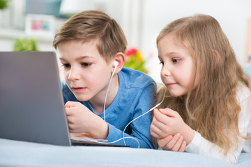 Two happy children playing with laptop and listening music with headphones