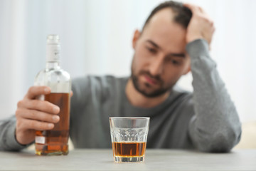 Fototapeta premium Glass with whisky on table and blurred man on background