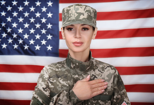 Female soldier holding hand on heart, with USA flag on background