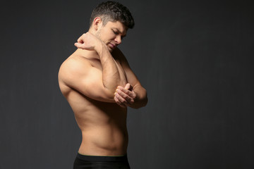 Young man suffering from pain in elbow on dark background