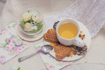 Fototapeta na wymiar Afternoon tea time party. White cup of green light tea with cakes raisin, chocolate cookies in shabby chic elegant traditional interior on lace napkin with pink flowers. Cookie heart shape. 