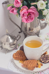 Afternoon tea time party. White cup of green light tea with cakes raisin, chocolate cookies in shabby chic elegant traditional interior on lace napkin with pink flowers. Cookie heart shape. 