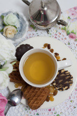 Afternoon tea time party. White cup of green light tea with cakes raisin, chocolate cookies in shabby chic elegant traditional interior on lace napkin with pink flowers. Cookie heart shape. 