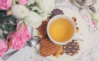 Obraz na płótnie Canvas Afternoon tea time party. White cup of green light tea with cakes raisin, chocolate cookies in shabby chic elegant traditional interior on lace napkin with pink flowers. Cookie heart shape. 