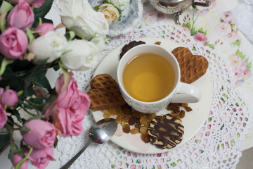 Obraz na płótnie Canvas Afternoon tea time party. White cup of green light tea with cakes raisin, chocolate cookies in shabby chic elegant traditional interior on lace napkin with pink flowers. Cookie heart shape. 