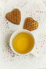 Happy Valentines day tea time or love party. White cup of green tea with cakes raisin chocolate cookies in shabby chic elegant traditional interior, lace napkin with pink flowers. Cookie heart shape.