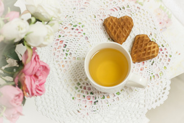 Happy Valentines day tea time or love party. White cup of green tea with cakes raisin chocolate cookies in shabby chic elegant traditional interior, lace napkin with pink flowers. Cookie heart shape.