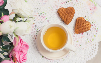 Fototapeta na wymiar Happy Valentines day tea time or love party. White cup of green tea with cakes raisin chocolate cookies in shabby chic elegant traditional interior, lace napkin with pink flowers. Cookie heart shape.