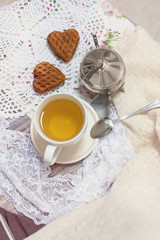 Happy Valentines day tea time or love party. White cup of green tea with cakes raisin chocolate cookies in shabby chic elegant traditional interior, lace napkin with pink flowers. Cookie heart shape.