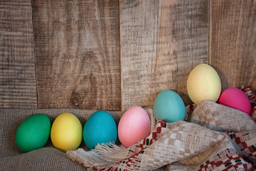 Easter colored eggs with bow against natural wooden textured background on linen fabric. Rustic vintage country style. Happy easter background concept.