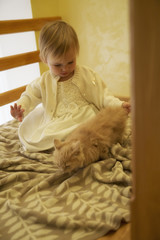 Little girl in the white dress playing with a kitten