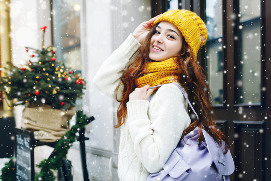 Outdoor waist up portrait of young beautiful happy smiling girl walking on street. Model looking at camera, wearing stylish winter clothes, accessories, holding backpack. Empty, copy space for text