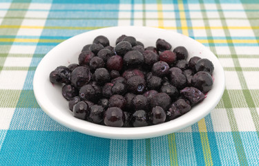 Frozen blueberries in a white bowl on a cloth place mat.