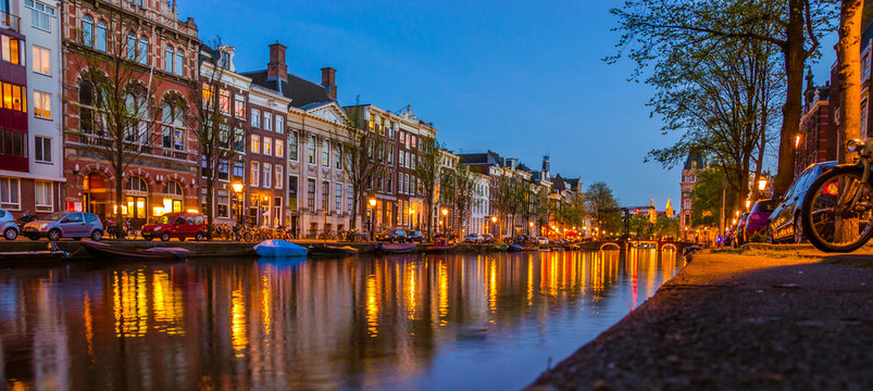 Traditional old buildings and boats at night in Amsterdam, Netherlands.