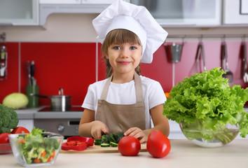 Small girl chef cutting vegetables in kitchen