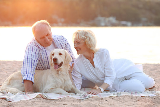 Senior couple and big dog sitting on plaid on riverside