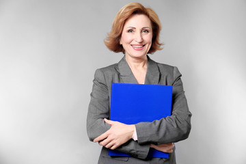 Attractive senior woman holding folder on grey background