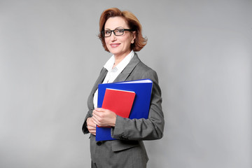 Portrait of attractive senior woman holding folder on grey background