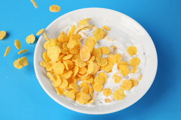 Corn flakes with milk in bowl on blue background