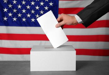 Fototapeta na wymiar Male hand putting voting ballot into the box on American flag background