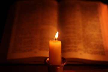 Burning candle and Bible on background