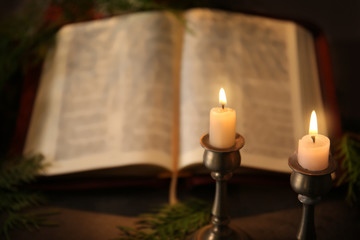 Closeup view of burning candles with blurred open Bible on background