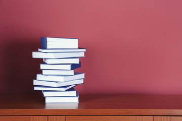 Pile of books on wooden table against pink background